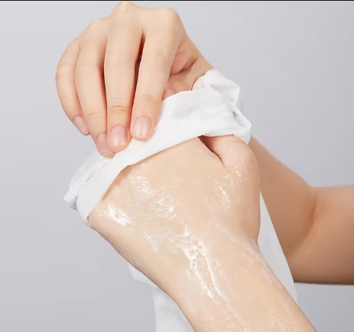 Hand applying a white cream or lotion to another hand on a light gray background