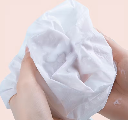 White cotton pad held between fingers on a light pink background