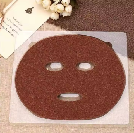 Brown face mask on a clear sheet with flowers and text in the background