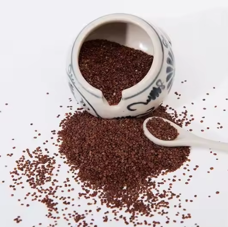 Ceramic bowl with a spoonful of brown seeds on a white background